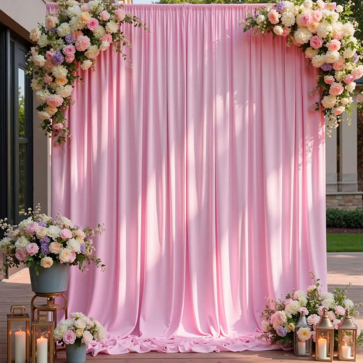 A pink draped backdrop for an event featuring floral arrangements and lanterns.