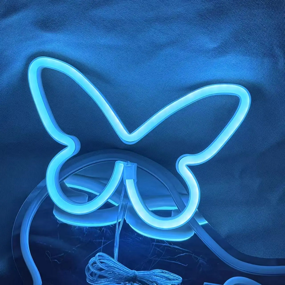 A glowing blue neon sign shaped like a butterfly is displayed against a dark blue fabric background.