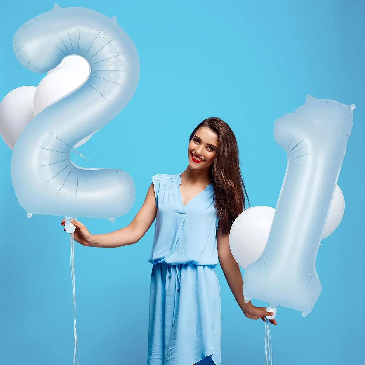 A woman holds up a large light blue foil number balloon shaped like the number 2 against a blue background.