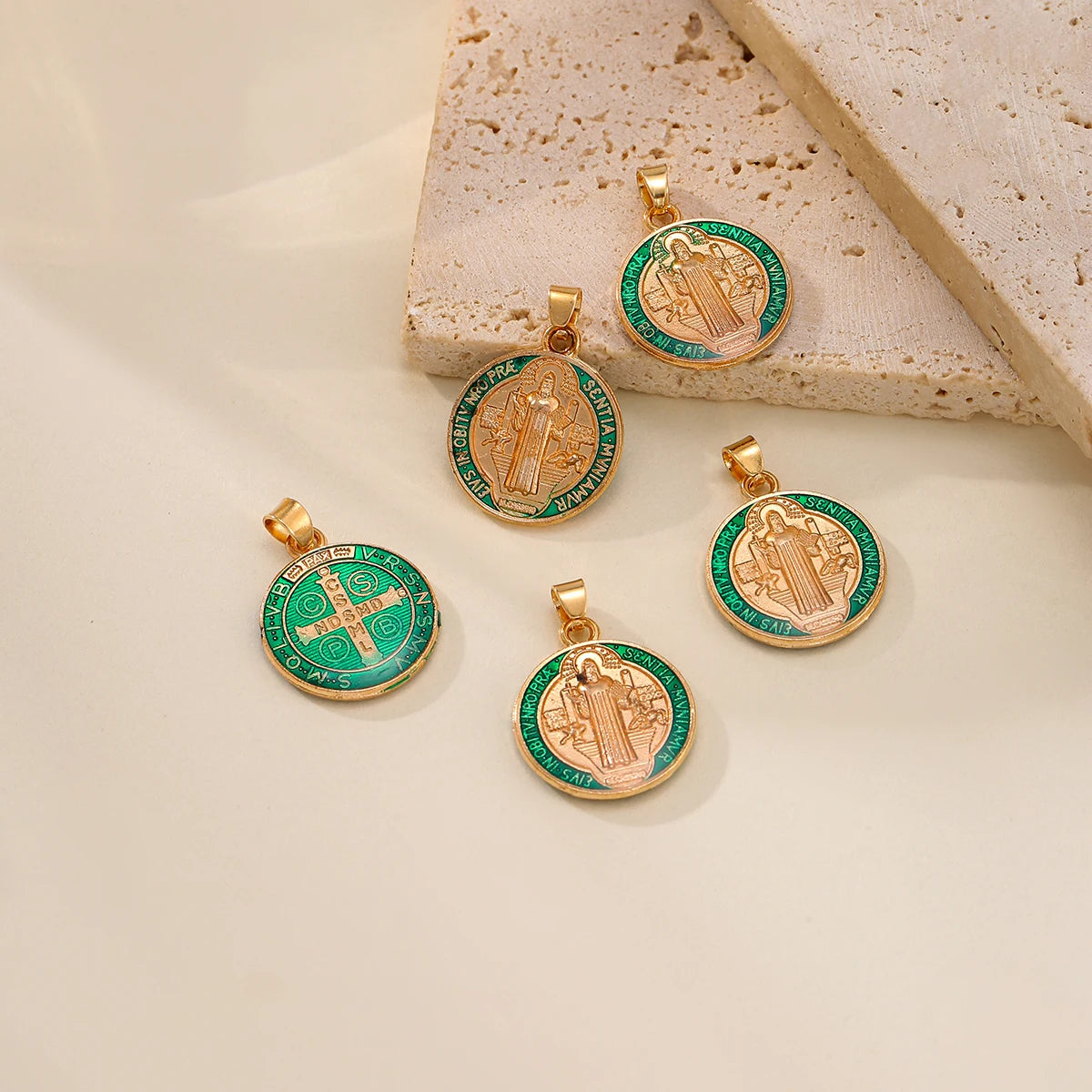 A set of gold-toned St. Benedict medals with green enamel and a cross pendant displayed on a light background.