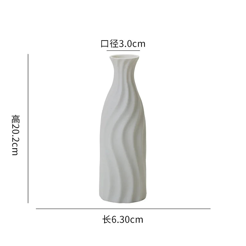A tall, white ceramic desktop vase featuring an organic ripple design.