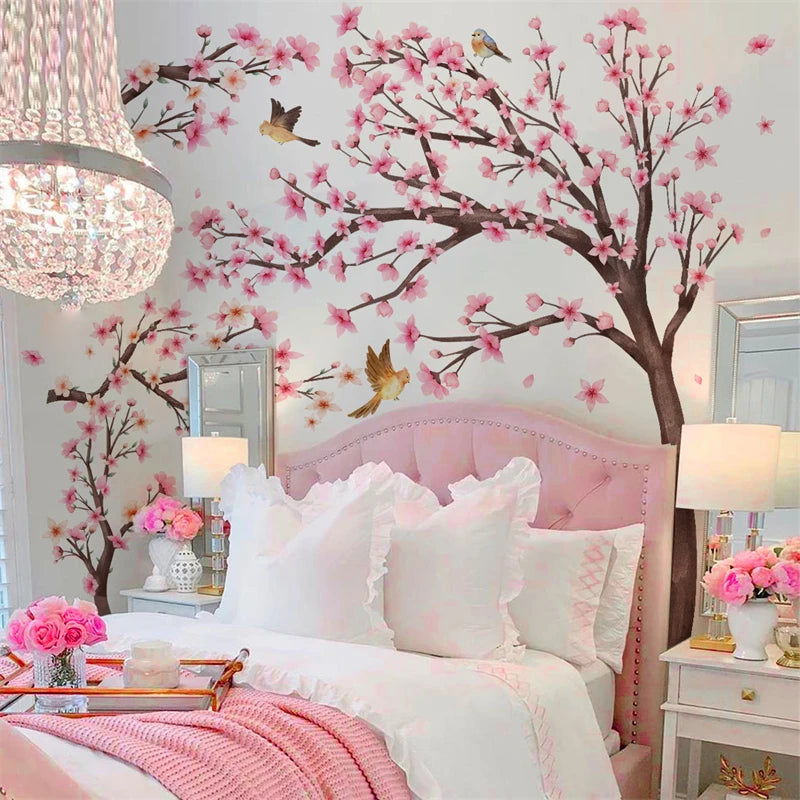 A bedroom decorated with pink cherry blossom tree wall stickers, featuring a pink upholstered bed and white linens.