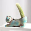 A ceramic succulent planter shaped like a cat holding a tall, fuzzy green cactus plant.