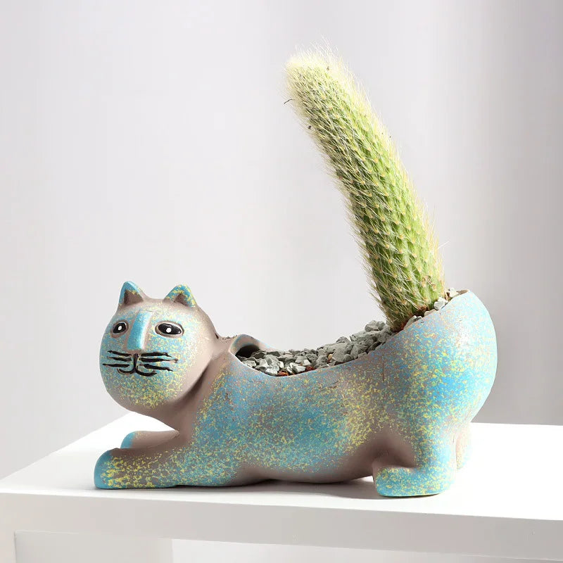 A ceramic succulent planter shaped like a cat holding a tall, fuzzy green cactus plant.