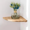 A glass vase filled with blue and green flowers sits on a natural wooden corner floating shelf.