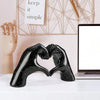 Black heart-shaped resin hand sculpture with a speckled finish resting on a white desk.