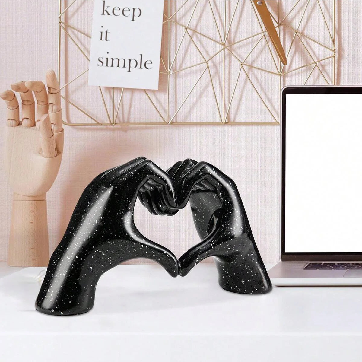 Black heart-shaped resin hand sculpture with a speckled finish resting on a white desk.