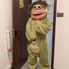 A plush monster costume in lime green coral fleece with large eyes and a pink snout, hanging on a door.