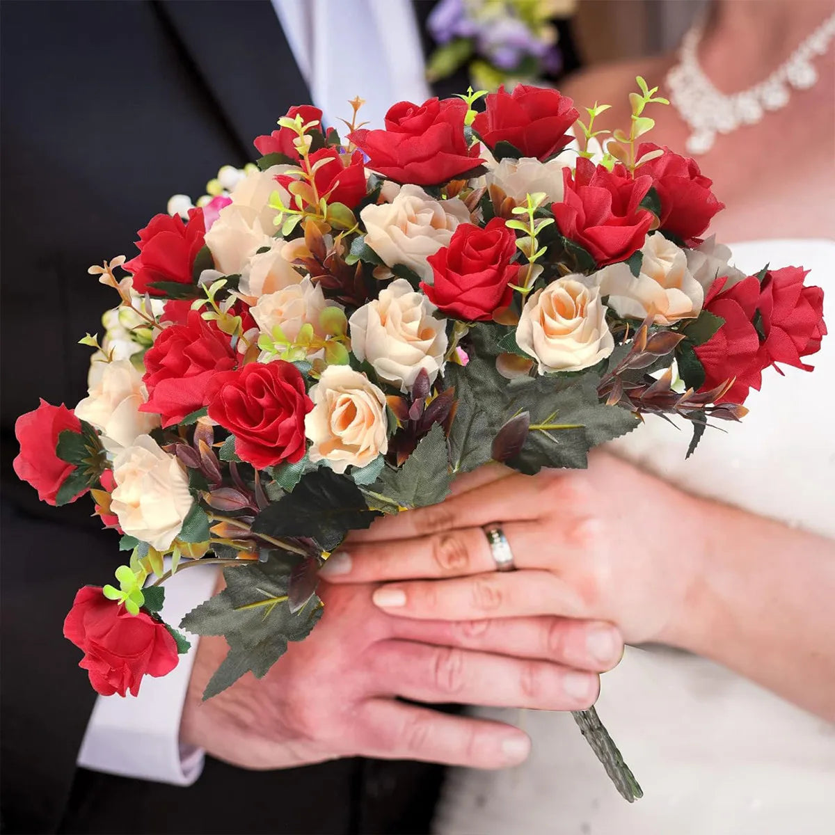 A bouquet of red and cream silk rose flowers held by a person in a wedding dress.