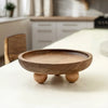 A round wooden storage tray with a shallow bowl and small feet resting on a white table.