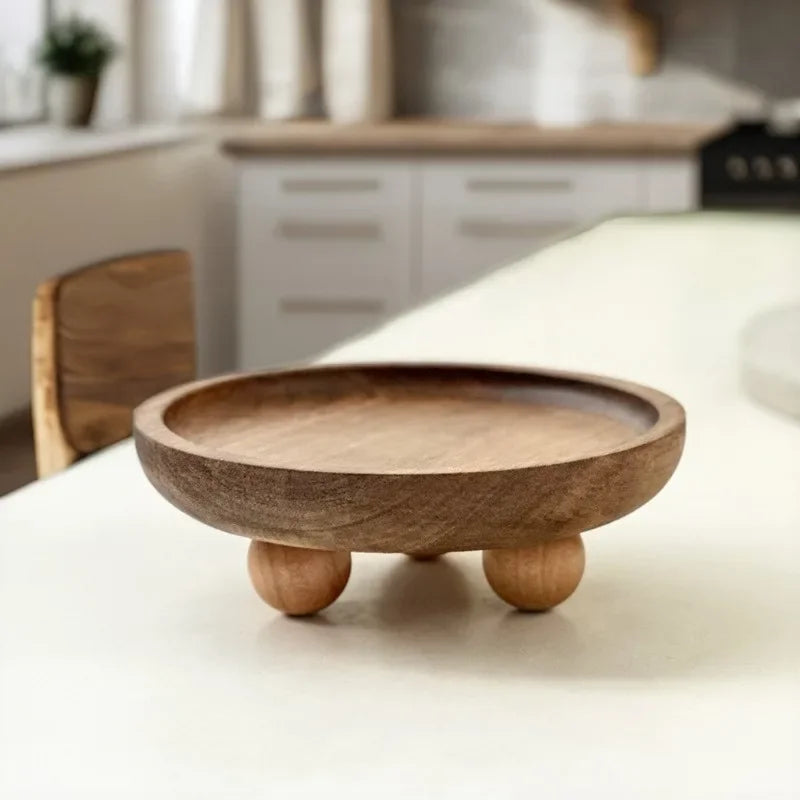 A round wooden storage tray with a shallow bowl and small feet resting on a white table.
