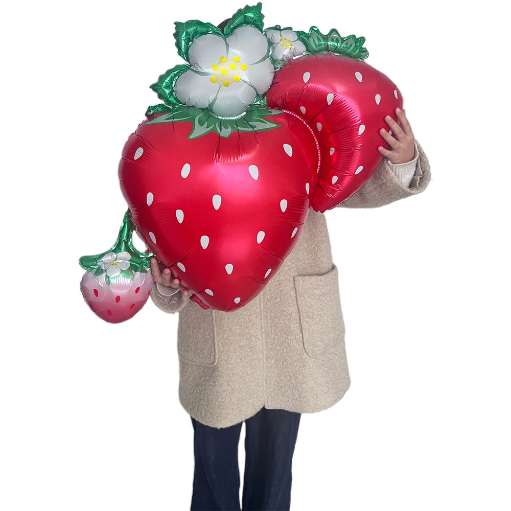 A person holds a cluster of red strawberry, green watermelon, and pink cherry themed party balloons.