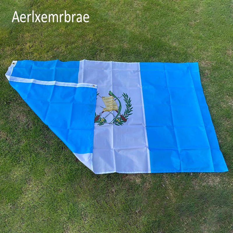 A large blue and white flag of Guatemala laid out on green grass.