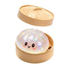 A light pink squishy toy shaped like a dumpling is displayed in its open cardboard container.