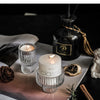 Porta-velas de vidrio transparente en color verde azulado con una vela de cera blanca, sobre una superficie oscura.
