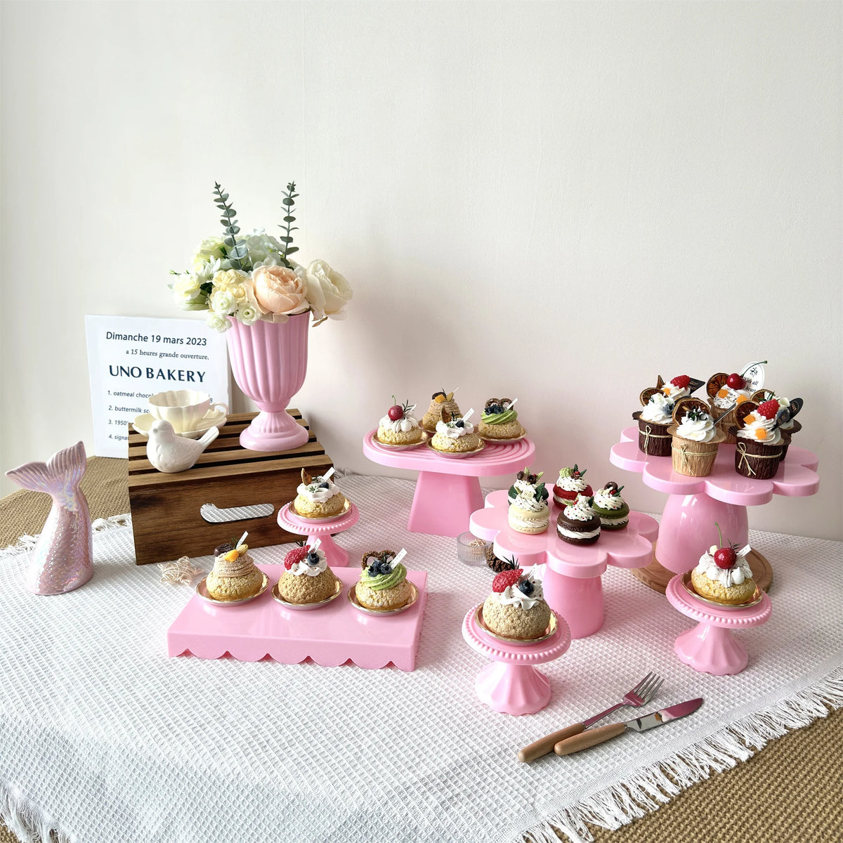 Two pink cupcake stands decorated with frosting and flowers on a white tablecloth.