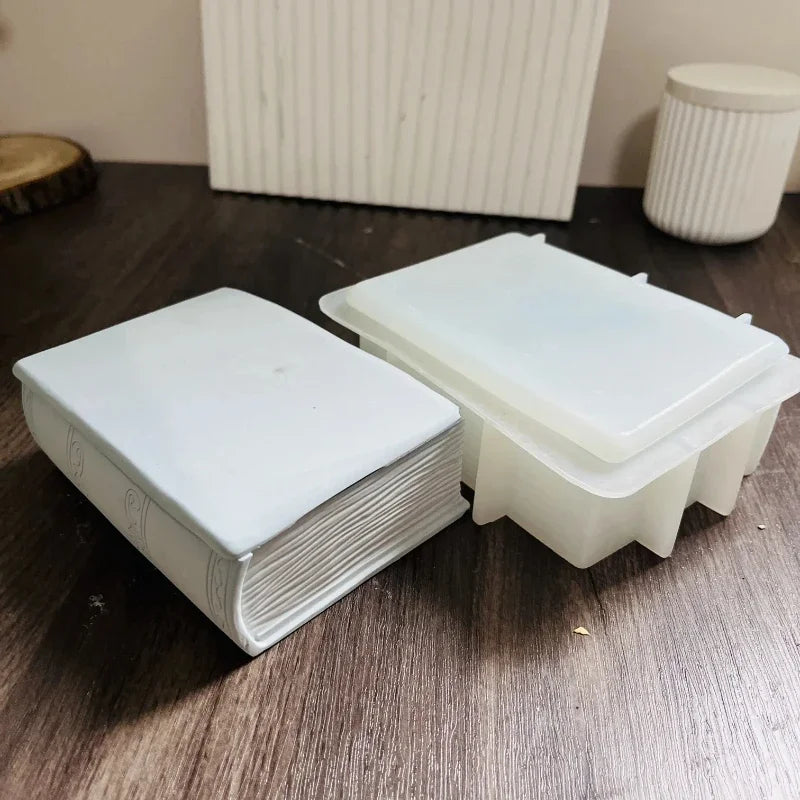 A white openable book-shaped silicone mold for resin and concrete DIY sits on a dark wooden surface.