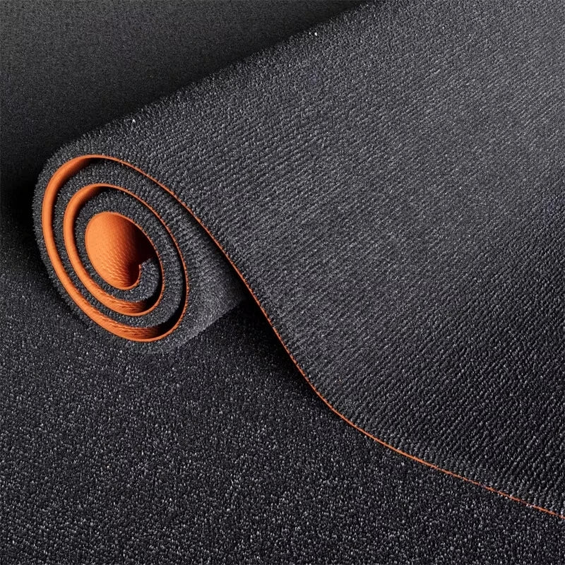 A roll of dark gray artificial grass carpet with an orange accent is shown on a black background.