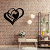 Black metal heart wall art with two intertwined hearts hanging on a brick wall above a wooden bench.