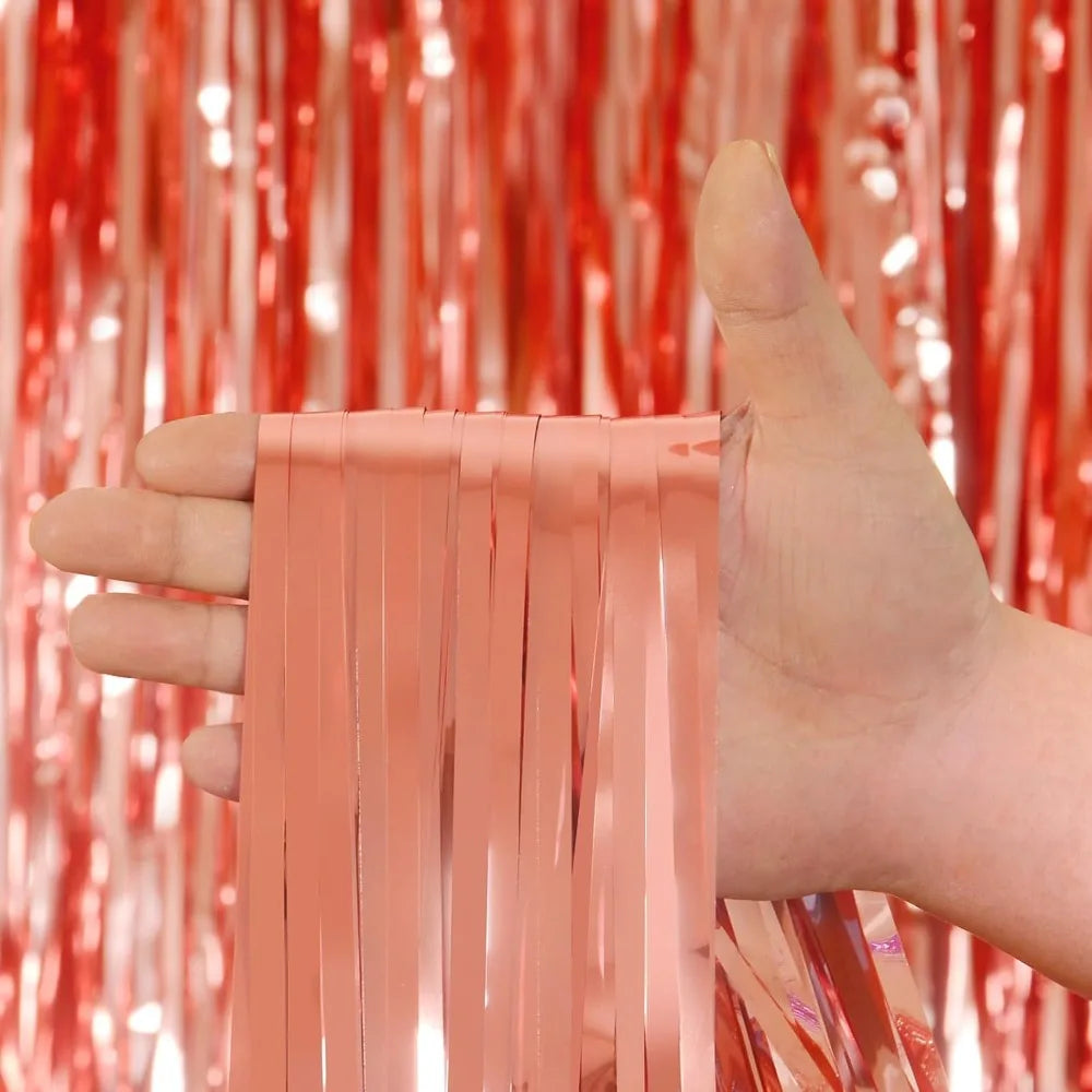 Une main tient une bande verticale de rideaux à franges roses contre un fond de rideaux à franges rouges.