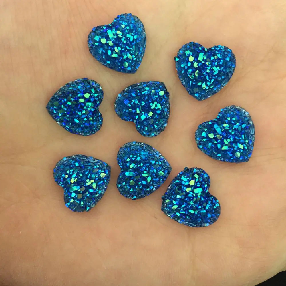 Eine Sammlung von zwölf blauen, herzförmigen Glitzer-Strasssteinen auf einer Hand.