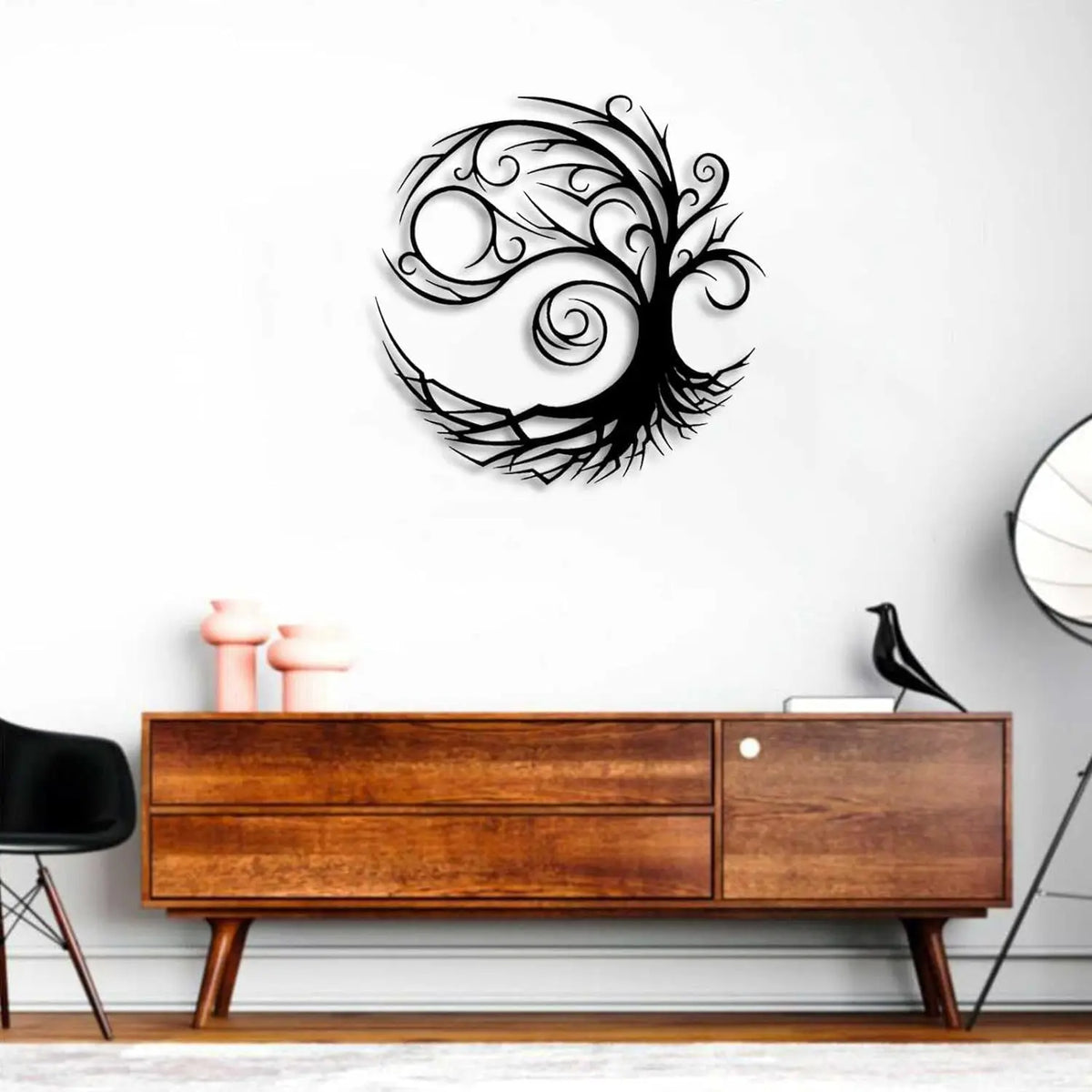 A black silhouette of a tree of life design mounted on a white wall above a wooden cabinet.