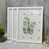 A set of three white wooden photo frames with green palm leaf illustrations for wall decor.