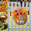 A decorative plastic pumpkin door hanger set is displayed on a white picket fence with autumn foliage.