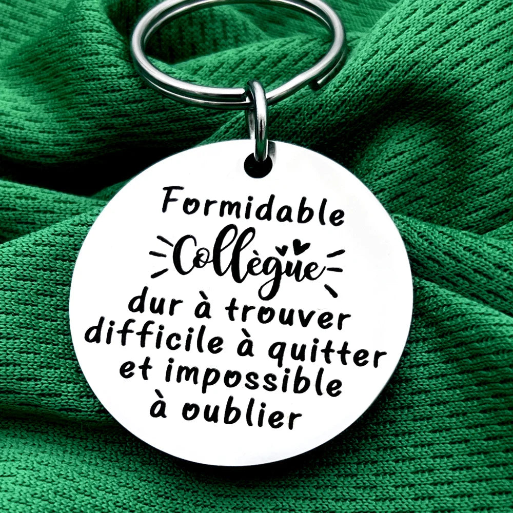 Silver keychain with a white disc engraved with the French quote: Formidable collègue dur à quitter et impossible à oublier