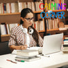 A woman wearing headphones is working on a laptop in a library setting with a neon sign reading CALMING CORNER.