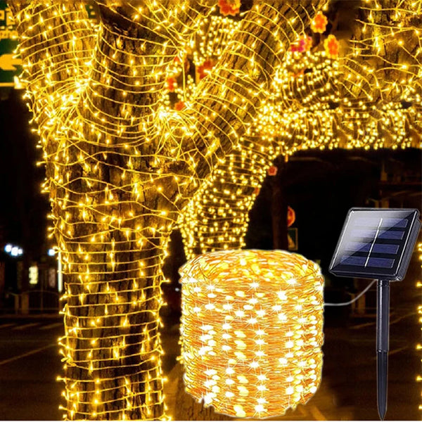 A close-up of a tree and a cylindrical light fixture wrapped in warm yellow fairy string lights for outdoor decoration.