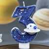 A blue glitter number three candle decorated with stars and a white planet design.