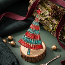A handcrafted wooden Christmas tree decorated with red and blue rhinestones, resting on a green surface.