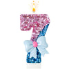 A large number candle shaped like a 7, decorated with pink and blue glitter, topped with a flame and tied with a light blue b