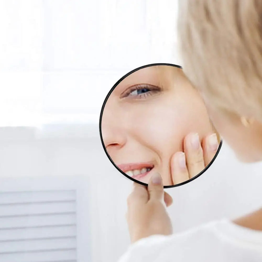 A woman uses a 50x magnifying compact mirror with a suction cup to examine her skin.