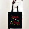 Black tote bag featuring red text that reads Christmas and Happy with green holly accents