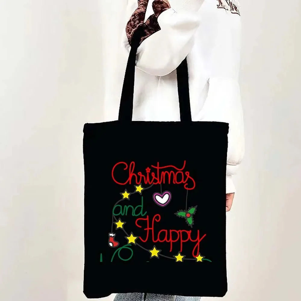 Black tote bag featuring red text that reads Christmas and Happy with green holly accents