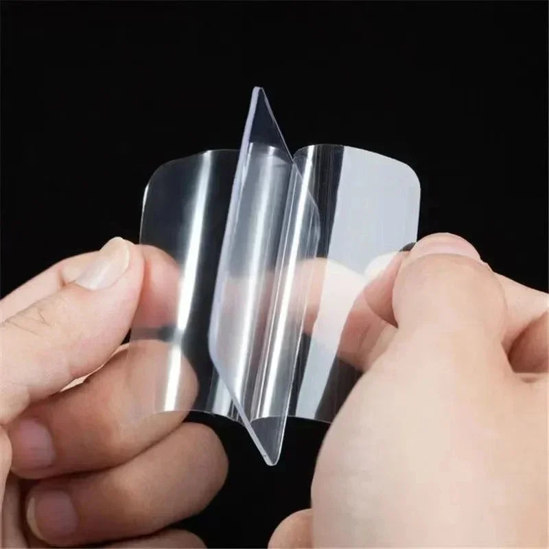 Hands hold a clear double-sided adhesive tape, showing its transparent and flexible nature.