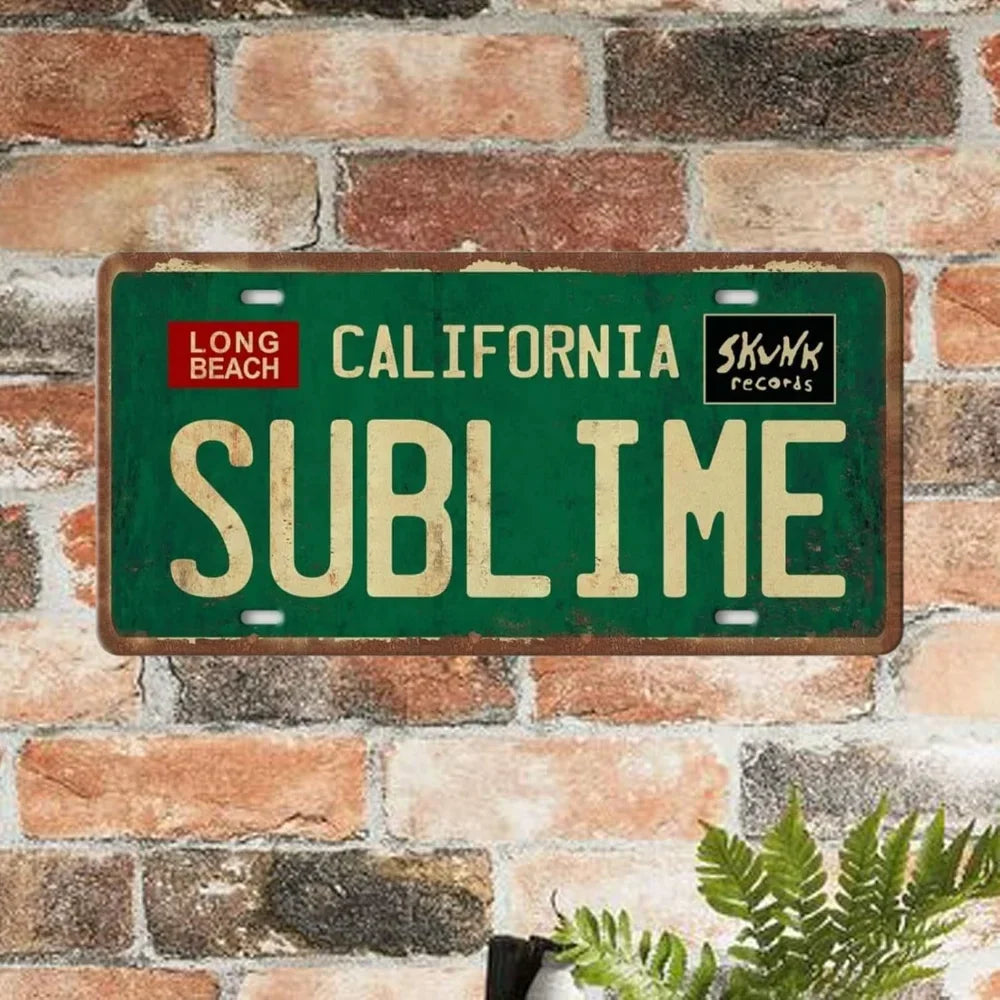 A vintage metal wall sign with the word SUBLIME in gold lettering on a dark green background mounted on a brick wall.