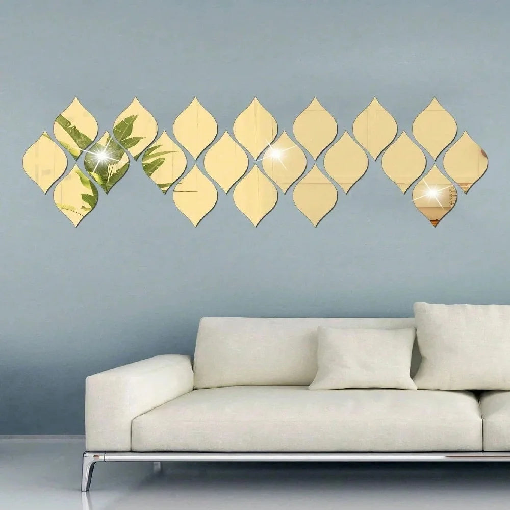 A set of ten gold reflective acrylic droplet mirror stickers arranged in a wavy line on a light blue wall above a modern sofa