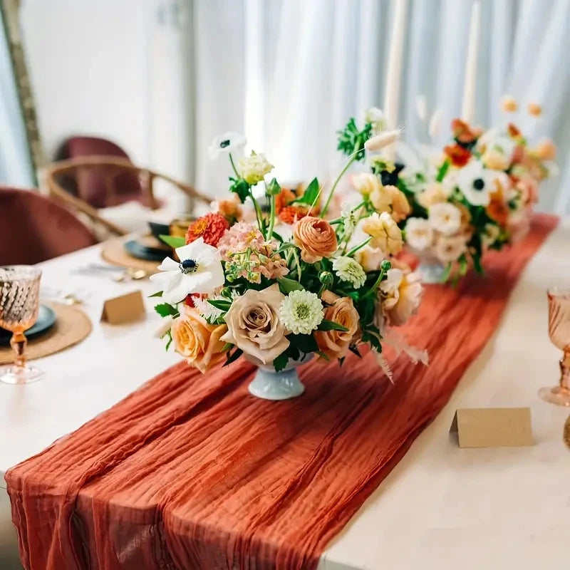A close-up of a floral centerpiece on a table with an orange linen runner and candles.