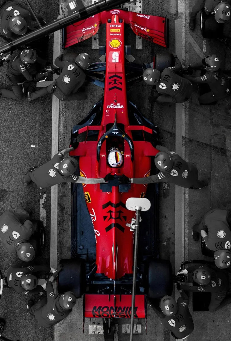 A close-up view of a red and black Formula 1 racing car model on a gray concrete surface.
