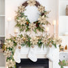 A wreath of dried flowers and greenery hangs above a white fireplace mantel decorated with white socks.