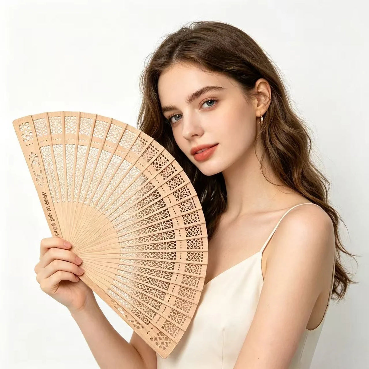 A woman holds a light wood folding fan with intricate cutouts against a white background.