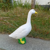 A white garden statue of a goose with yellow beak standing on a gray pavement.