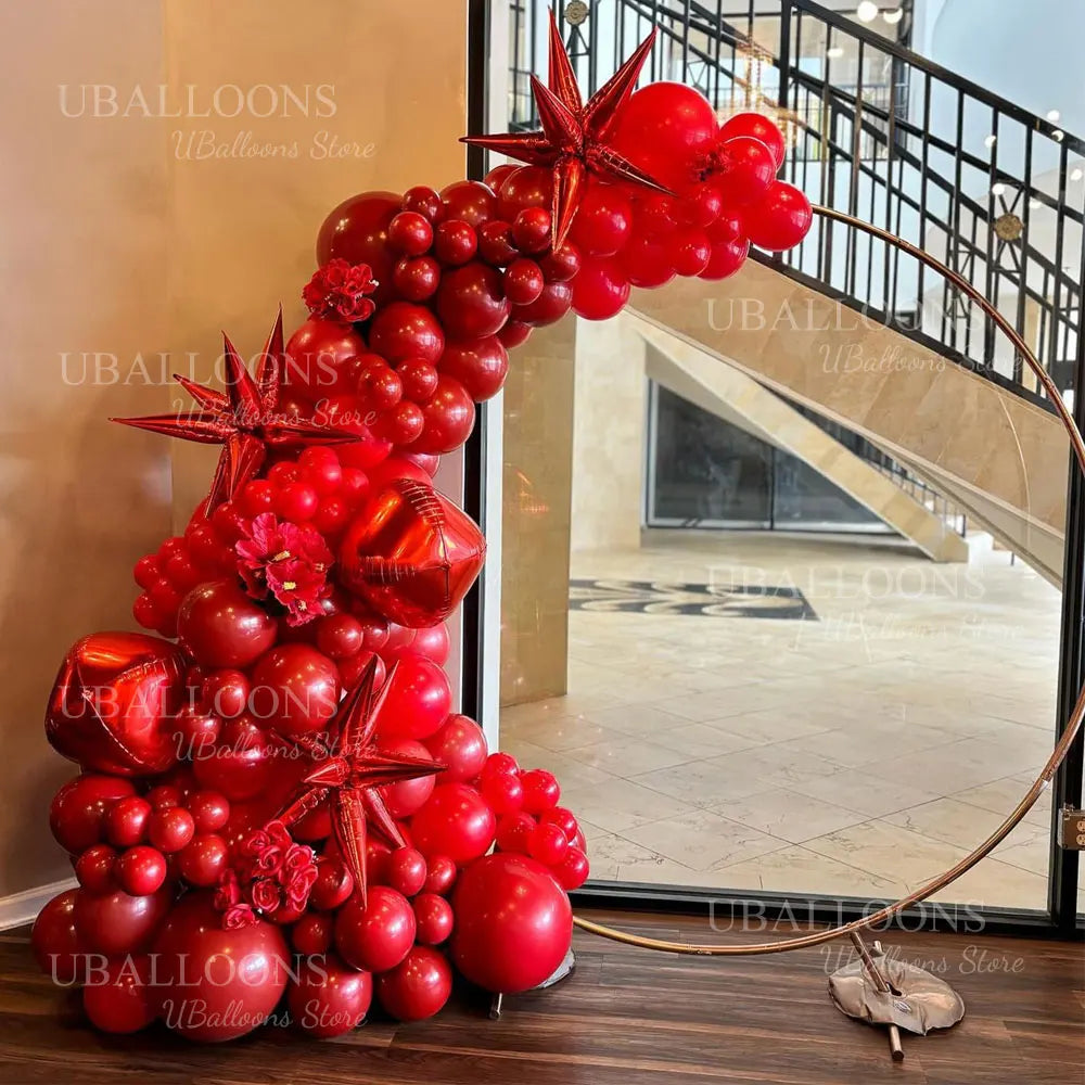 A large arrangement of deep burgundy latex balloons shaped like stars and clusters is displayed on a wooden floor.