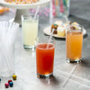A glass of orange juice sits next to a glass of lemonade and clear drinking straws on a gray surface.