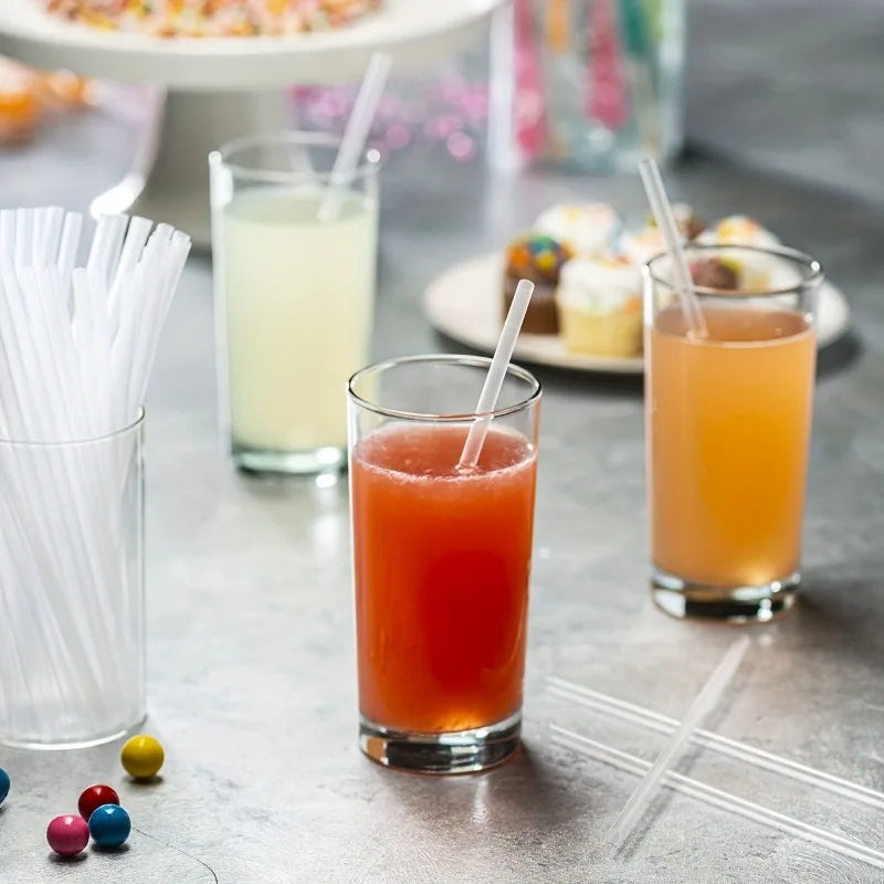 A glass of orange juice sits next to a glass of lemonade and clear drinking straws on a gray surface.