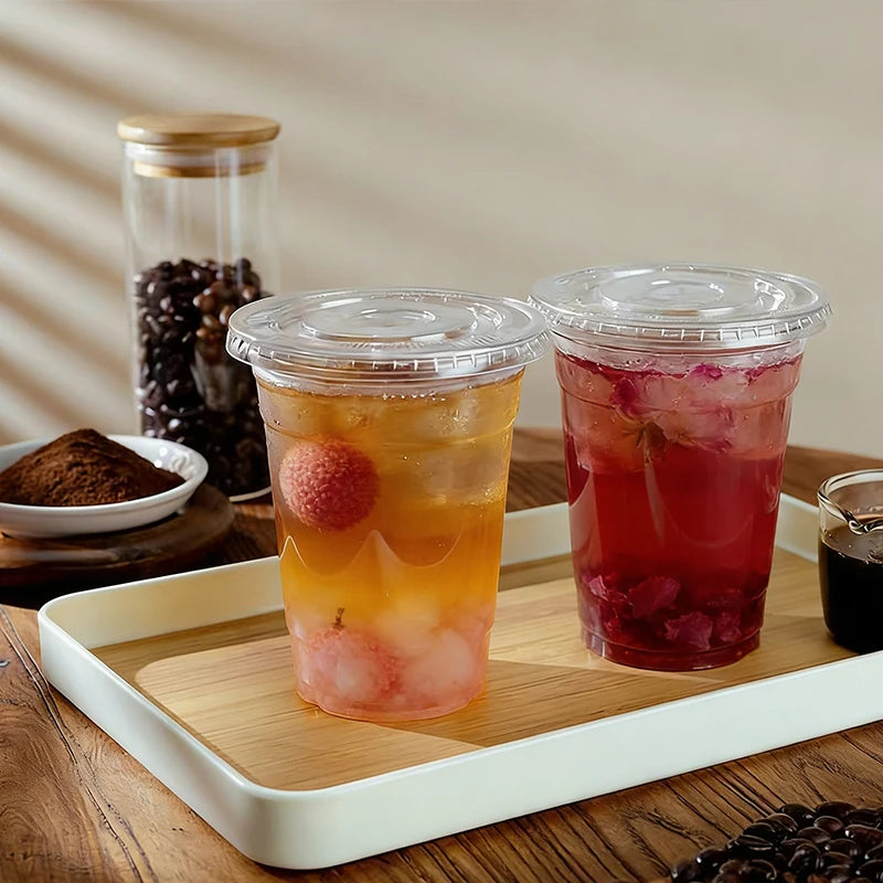 Three disposable plastic cups with lids containing various colored drinks on a wooden tray