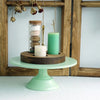 A metal cake stand displaying a glass jar filled with stacked cookies and a green candle.